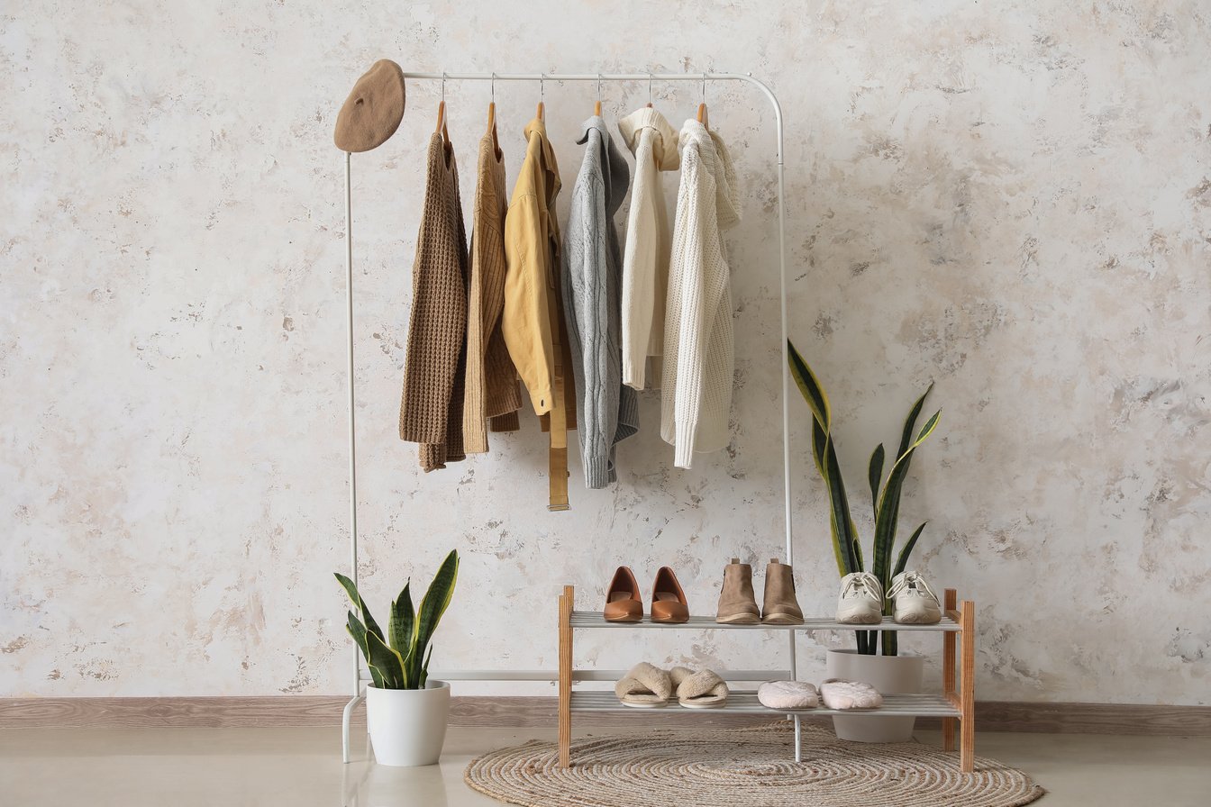 Rack with Warm Female Clothes, Shoes and Houseplants near Light Wall